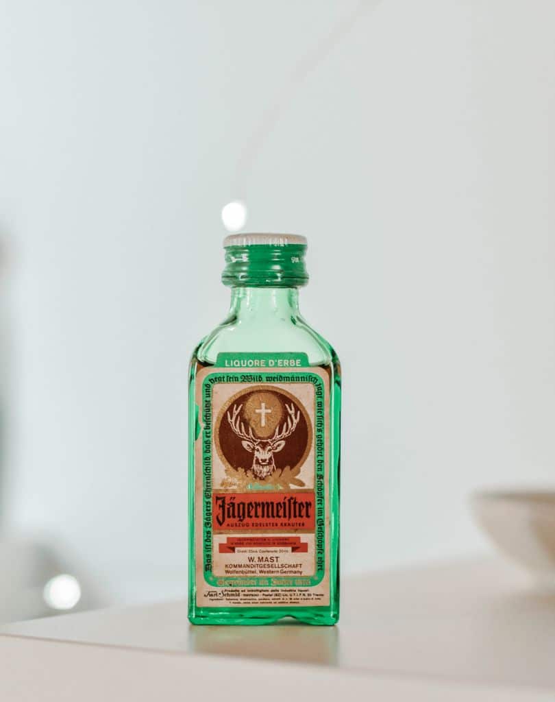 Close-up of a mini Jägermeister bottle on a shelf, indoors, bright lighting.